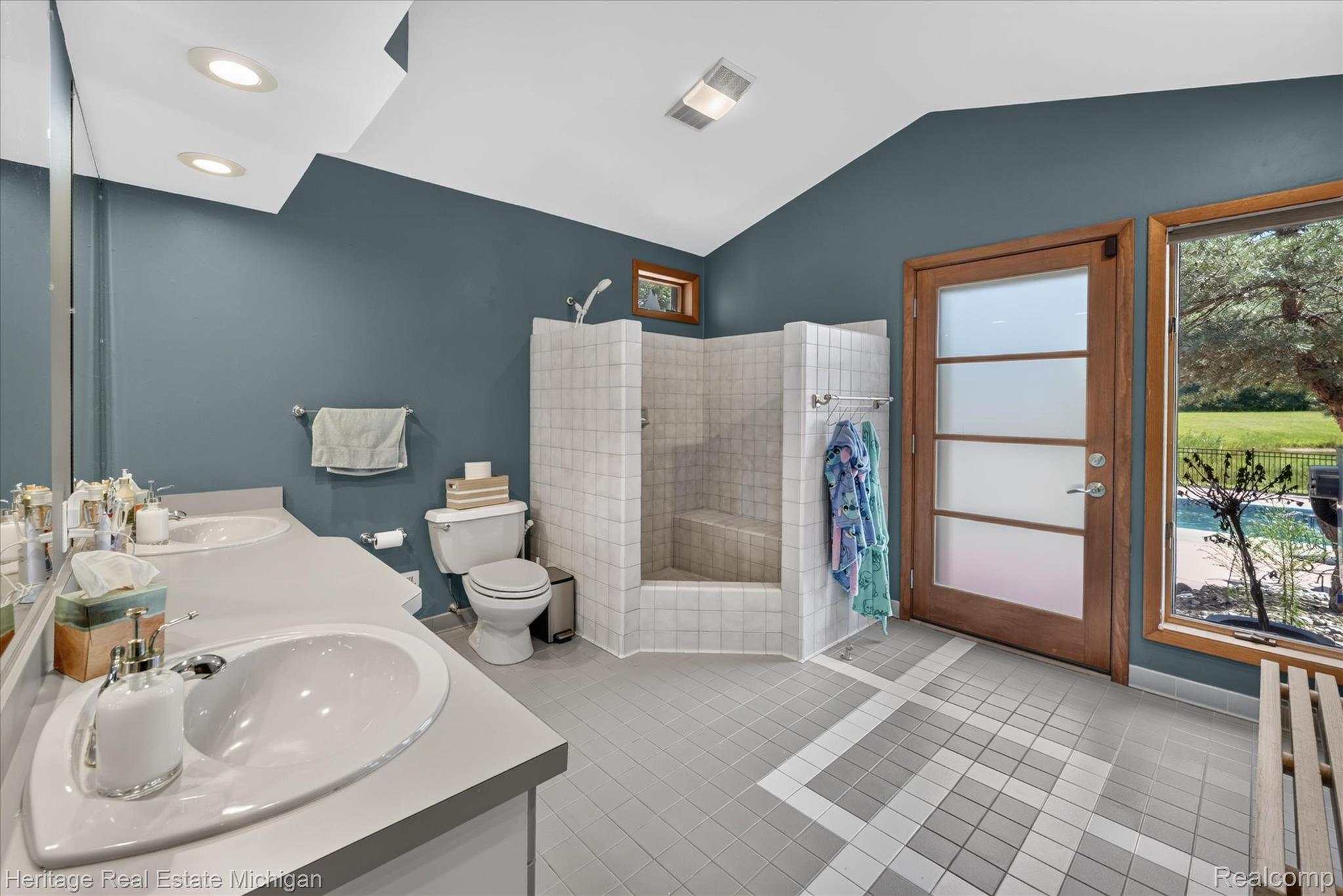 1888 Germany Road Williamston, MI 48895 - Photo 23 of 57 Spa-inspired primary bathroom showcasing a curved walk-in shower with tile surround, dual vanity with circular vessel sinks and gray countertops, and direct access to outdoor grounds through wood-frame French doors