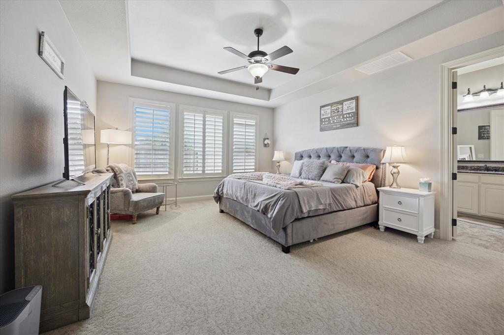 580 Butchart Drive Prosper, TX 75078 - Photo 16 of 40 Carpeted bedroom featuring a raised ceiling, connected bathroom, and a ceiling fan