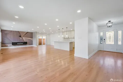 a view of an empty room and kitchen with wooden floor