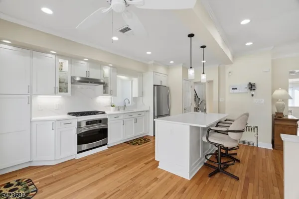 a kitchen with kitchen island a stove a sink a refrigerator and white cabinets with wooden floor