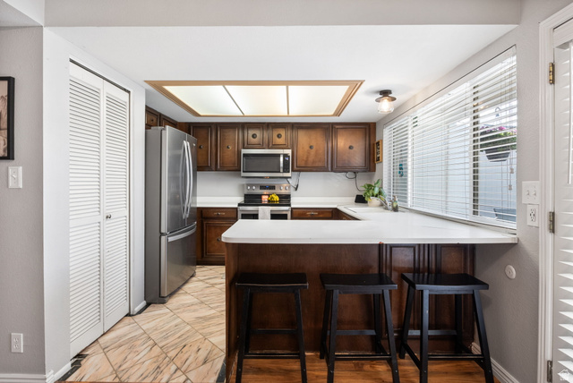 41 Benchmark Village Tooele, UT 84074 - Photo 7 of 26 Kitchen with light countertops, a breakfast bar area, a peninsula, stainless steel appliances, and dark wood finish cabinetry