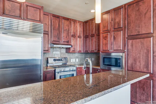a kitchen with stainless steel appliances granite countertop a refrigerator a stove and a sink with wooden cabinets