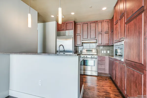 a kitchen with stainless steel appliances granite countertop a refrigerator a stove and a sink with wooden cabinets