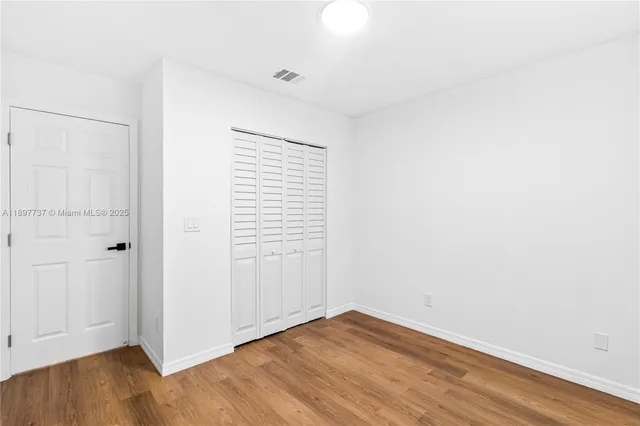 a view of an empty room with wooden floor and closet