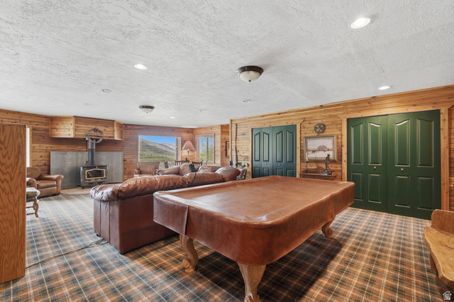 6 Beaver Springs Rancheros Oakley, UT 84055 - Photo 30 of 68 Spacious recreational room featuring wood paneling, a wood-burning stove with a stone surround, and large windows showcasing mountain scenery