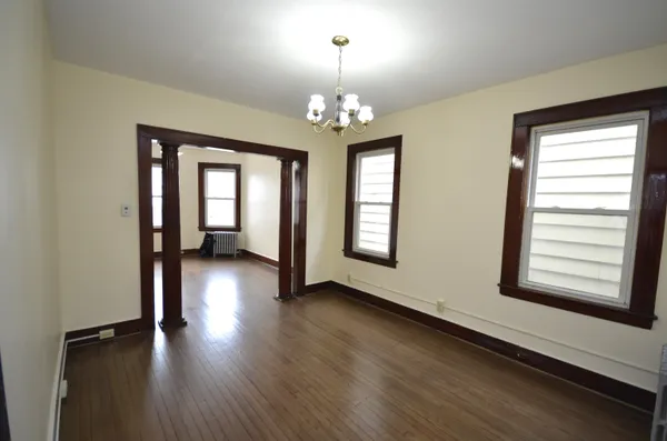 an empty room with wooden floor chandelier and windows