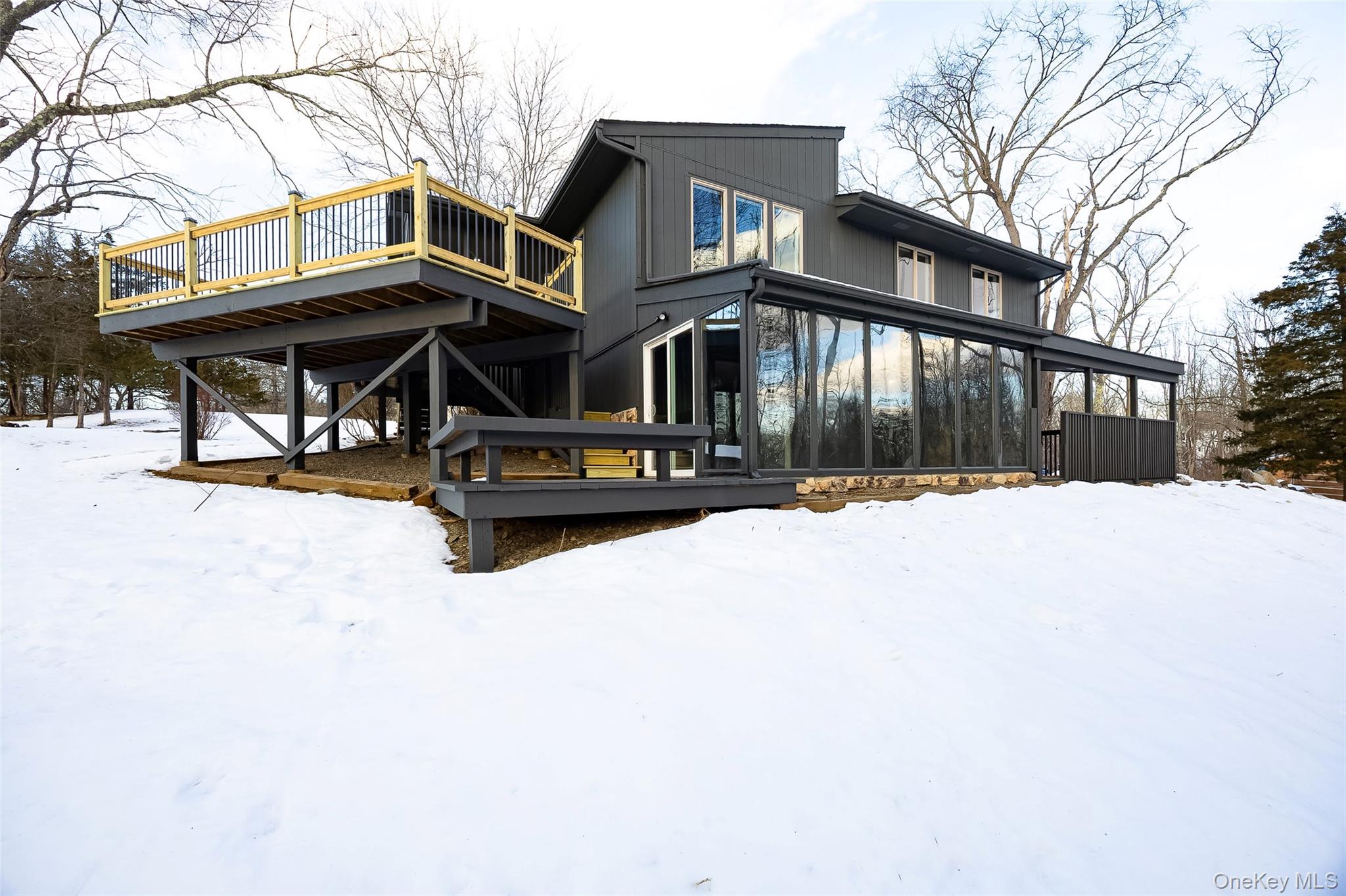 Snow covered back of property with a deck and a sunroom