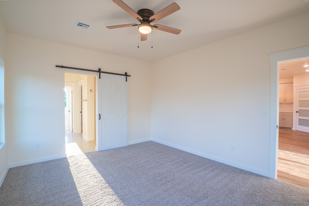 205 Blessings Way Colbert, OK 74733 - Photo 14 of 24 Carpeted interior space featuring a ceiling fan with integrated lighting, a white barn door on a black track, and white painted walls