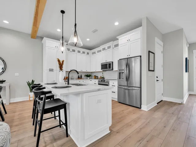 a kitchen with stainless steel appliances granite countertop a refrigerator a sink dishwasher a stove a dining table and chairs with wooden floor