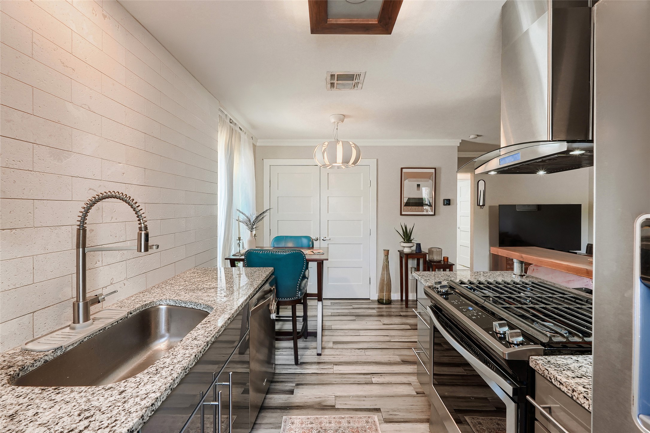5707 Tracy Lynn Lane, Unit A Austin, TX 78721 - Photo 17 of 33 Kitchen featuring stainless steel appliances, island range hood, crown molding, light wood-style floors, and light stone counters