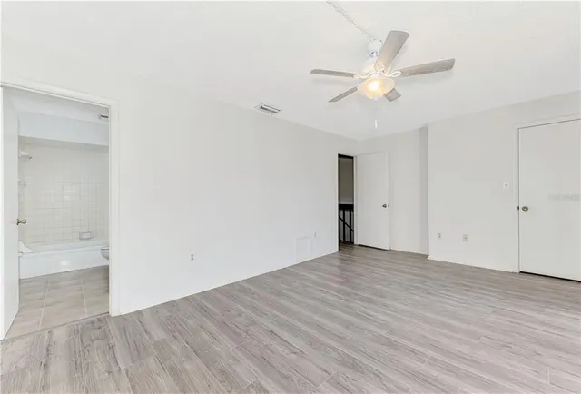 an empty room with wooden floor fan and windows