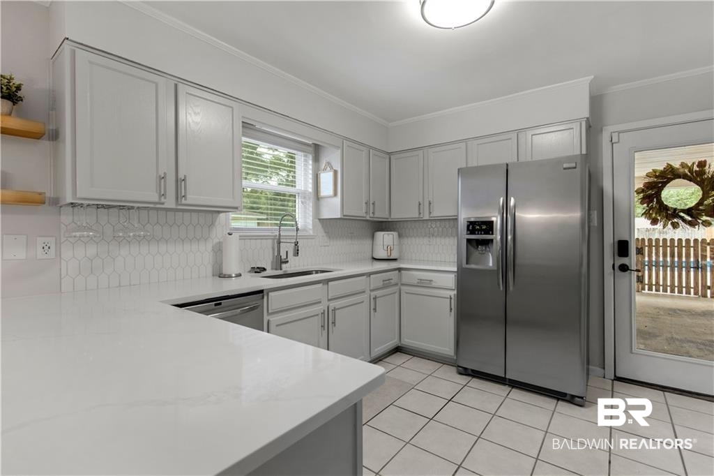 1624 Apex Drive Mobile, AL 36693 - Photo 13 of 29 Kitchen featuring decorative backsplash, stainless steel appliances, sink, crown molding, and light tile patterned floors
