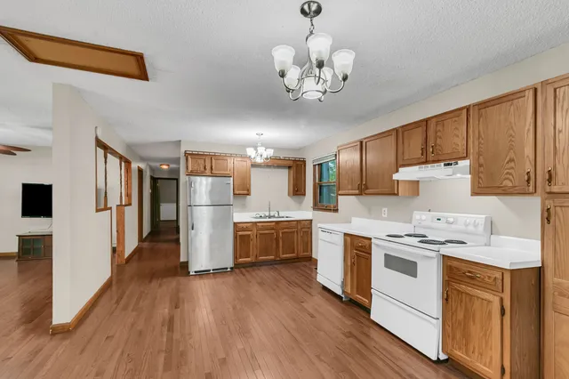 a kitchen with stainless steel appliances a stove top oven a refrigerator a sink dishwasher and white cabinets with wooden floor