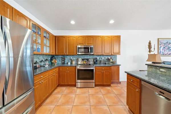 a kitchen with stainless steel appliances granite countertop a stove top oven a sink and dishwasher a refrigerator with wooden cabinets