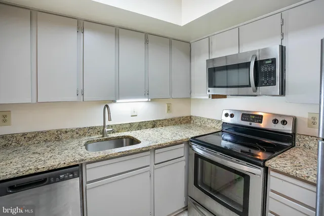 a kitchen with granite countertop a sink dishwasher stove and microwave with wooden cabinets
