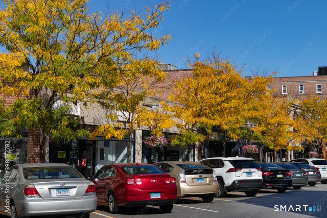 a view of road with card parked on side and retail shops