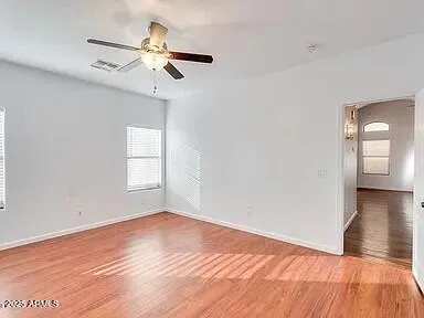 an empty room with wooden floor fan and windows