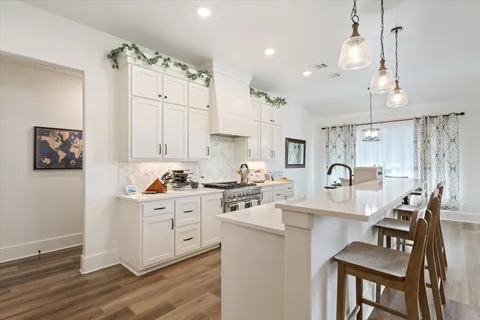 a kitchen with stainless steel appliances kitchen island granite countertop a stove top oven a sink a dining table and chairs with wooden floor