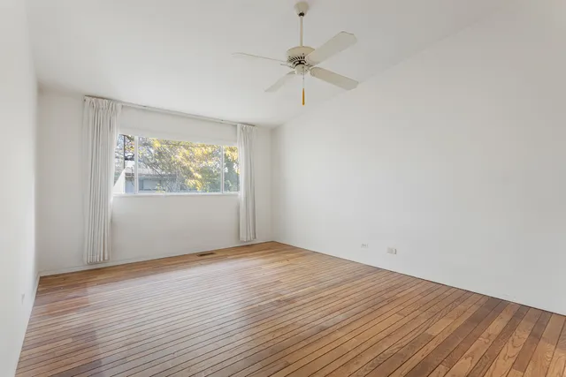an empty room with wooden floor chandelier fan and windows