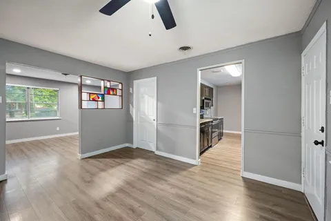 an empty room with wooden floor kitchen view and windows