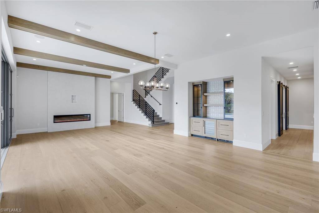 16728 Enclave Circle Naples, FL 34110 - Photo 11 of 49 Unfurnished living room with recessed lighting, beamed ceiling, light wood finished floors, and a glass covered fireplace