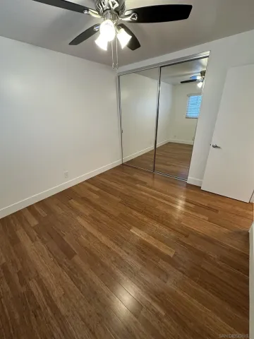 an empty room with wooden floor and fan