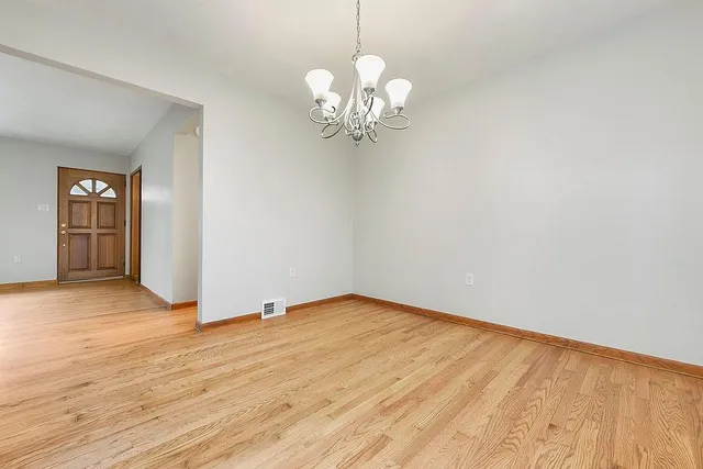a view of an empty room with chandelier and wooden floor