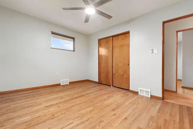 a view of an empty room with wooden floor and a ceiling fan