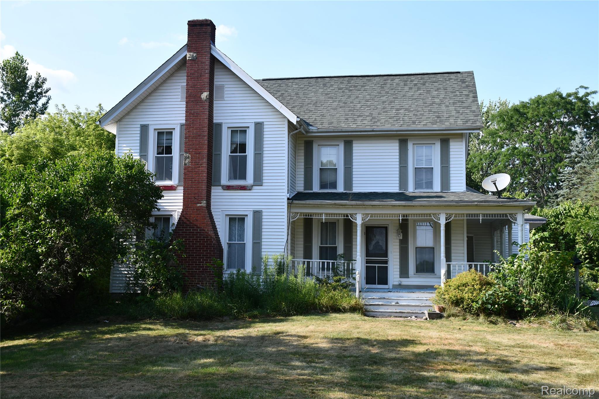 5245 East Clyde Road Howell, MI 48855 - Photo 2 of 28 Two-story residence featuring white siding, a prominent brick chimney, and a covered front porch with decorative railing