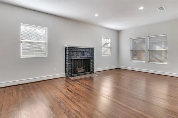 an empty room with wooden floor fireplace and windows