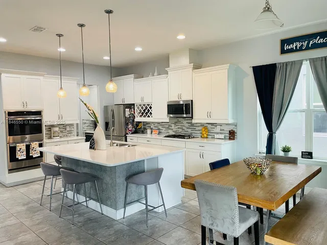a kitchen with stainless steel appliances kitchen island granite countertop a table chairs sink and cabinets
