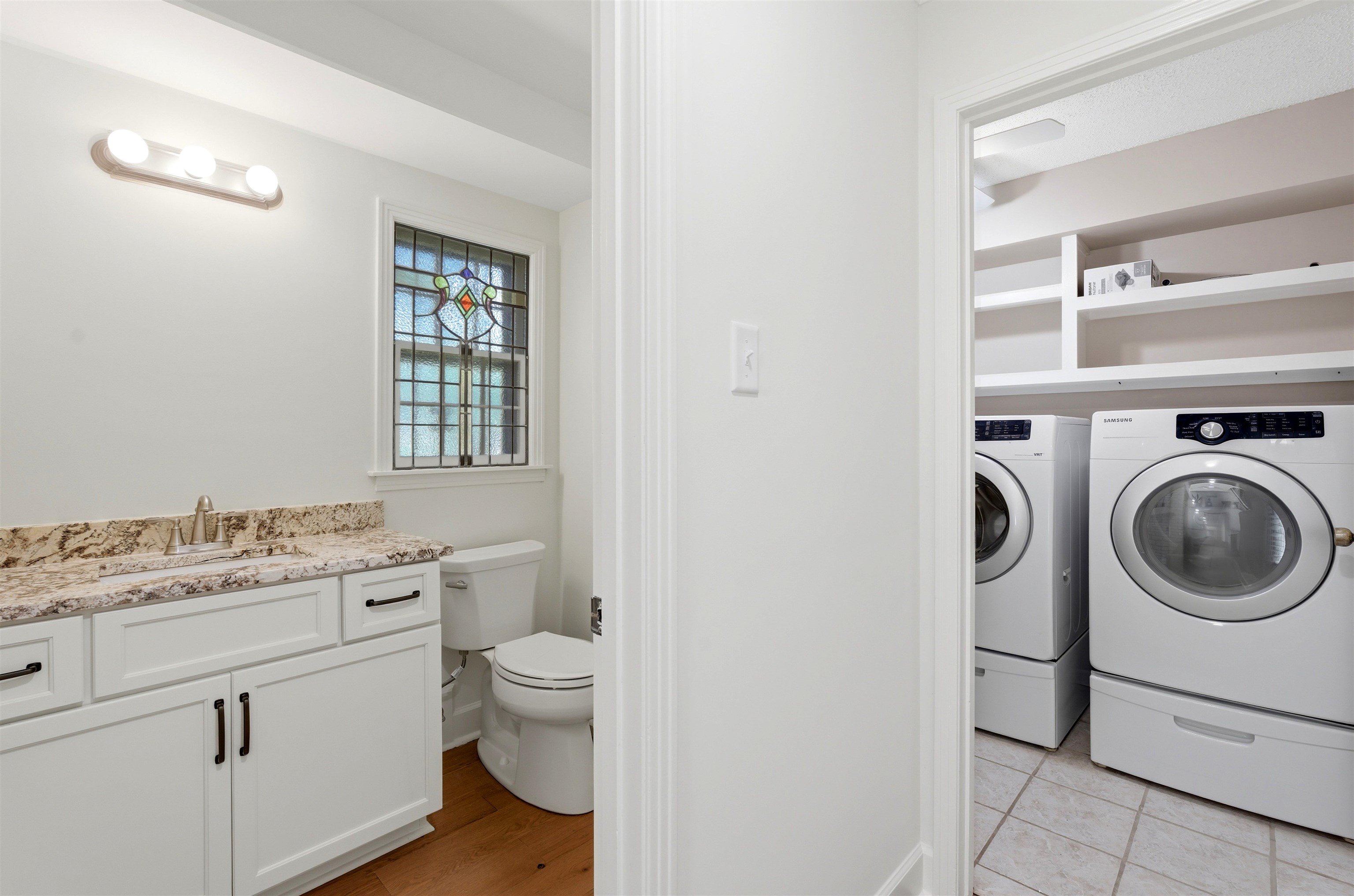 1984 Allenby Road Germantown, TN 38139 - Photo 34 of 37 Full-sized laundry machines with built-in shelving, contrasting with a nearby vanity featuring a stone countertop, an undermount sink, and a stained glass window