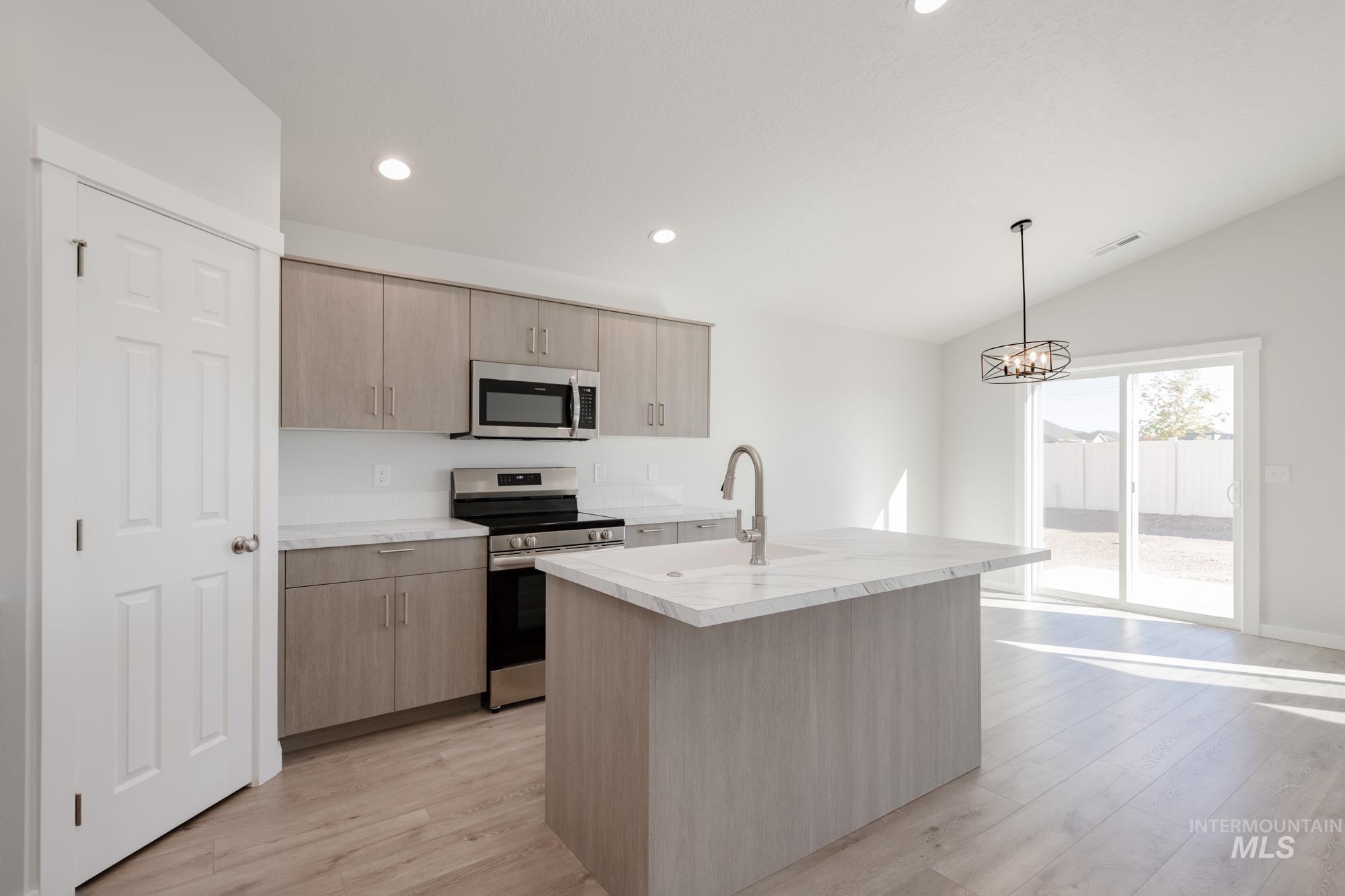 14092 Shiny Spruce Street Caldwell, ID 83607 - Photo 4 of 22 Modern kitchen featuring light wood-finish cabinetry, stainless steel appliances, and a central island with a sink and stone-look countertop
