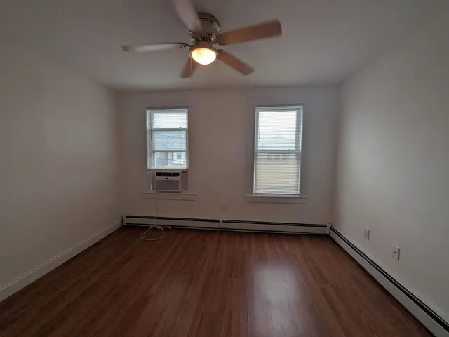 an empty room with wooden floor ceiling fan and windows