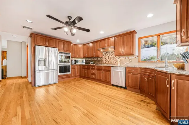 a large kitchen with stainless steel appliances granite countertop a stove a sink dishwasher and a refrigerator with wooden floor