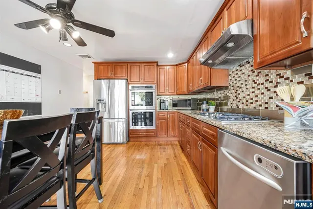 a kitchen with stainless steel appliances granite countertop a refrigerator a sink dishwasher a stove and white cabinets with wooden floor