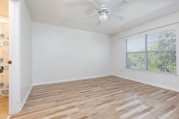 a view of an empty room with wooden floor and a ceiling fan