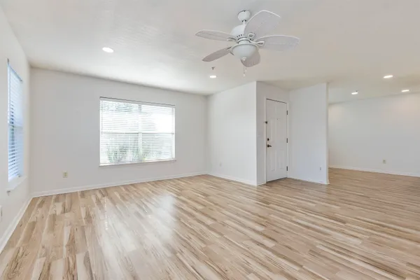 a view of an empty room with wooden floor and a ceiling fan