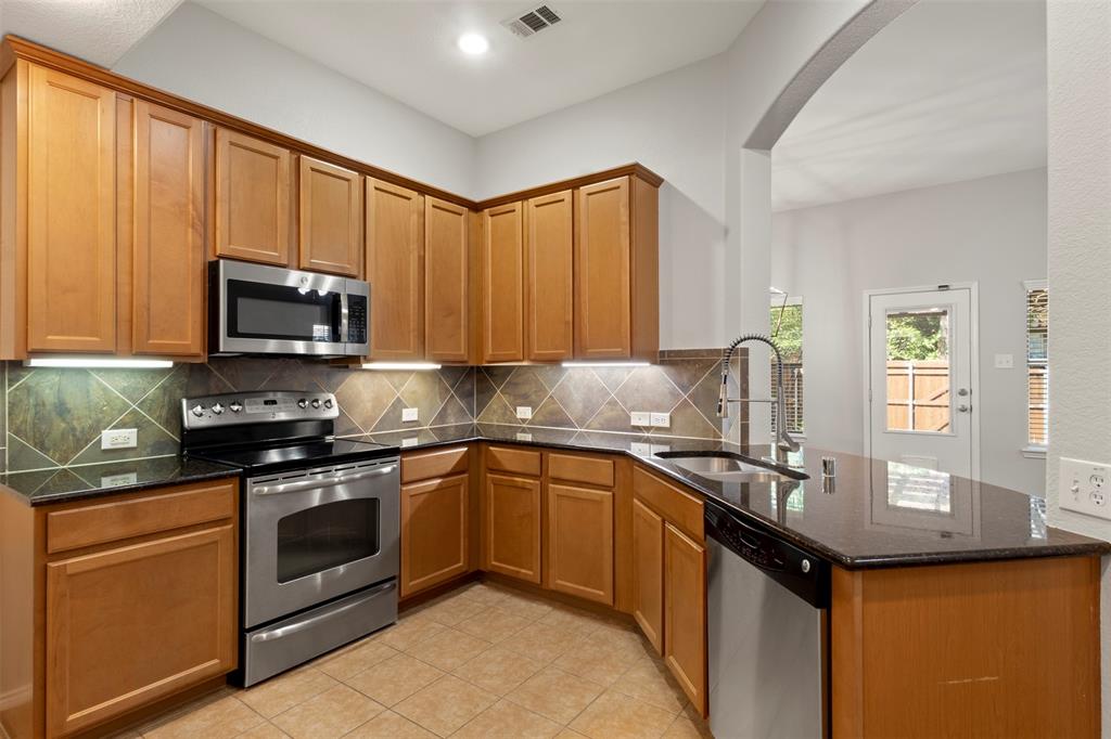 1034 Lucy Lane Allen, TX 75013 - Photo 4 of 16 Kitchen featuring stainless steel appliances, dark stone counters, brown cabinets, a peninsula, and tasteful backsplash