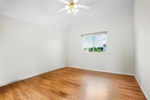an empty room with wooden floor chandelier fan and windows