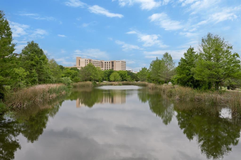 332 Adams Street Georgetown, TX 78628 - Photo 27 of 37 Reflecting the serene landscape, a peaceful pond anchors this picturesque setting with distant buildings framed by lush greenery.