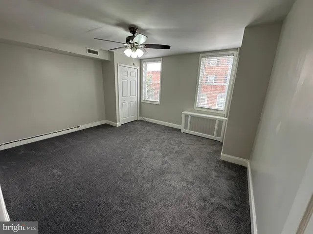 an empty room with chandelier fan and windows