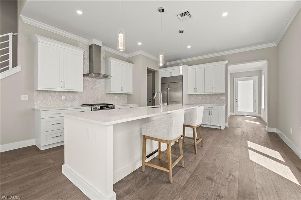 1134 Trail Terrace Drive Naples, FL 34103 - Photo 5 of 37 Kitchen featuring a large island with sink, wall chimney exhaust hood, stainless steel built in fridge, dark wood-style floors, and stove