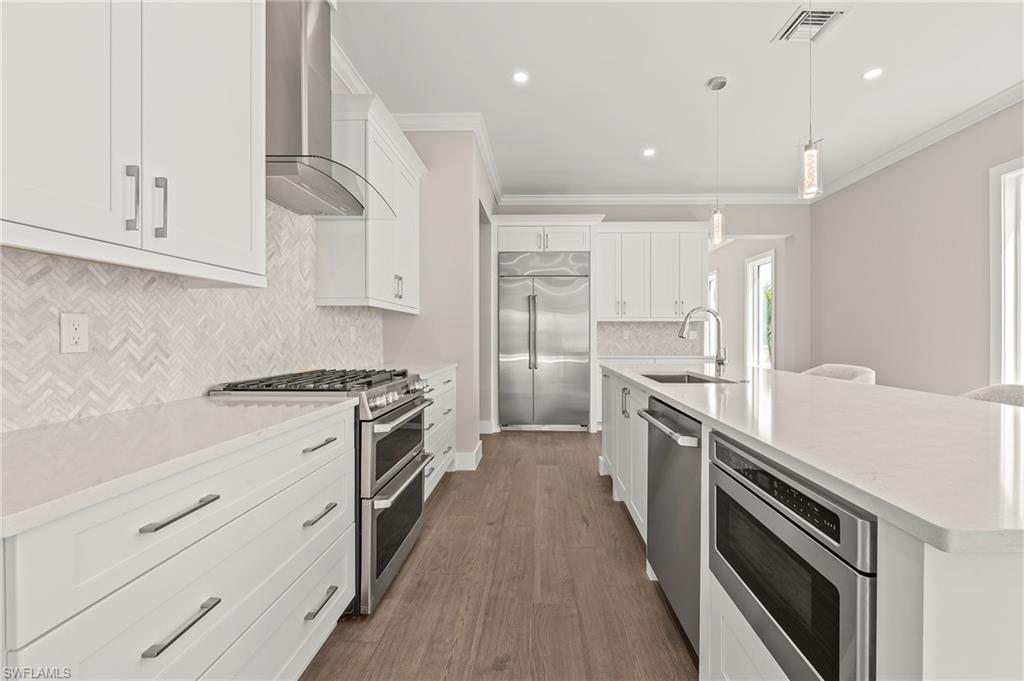 1134 Trail Terrace Drive Naples, FL 34103 - Photo 7 of 37 Kitchen featuring light countertops, ornamental molding, a sink, built in appliances, and wall chimney exhaust hood