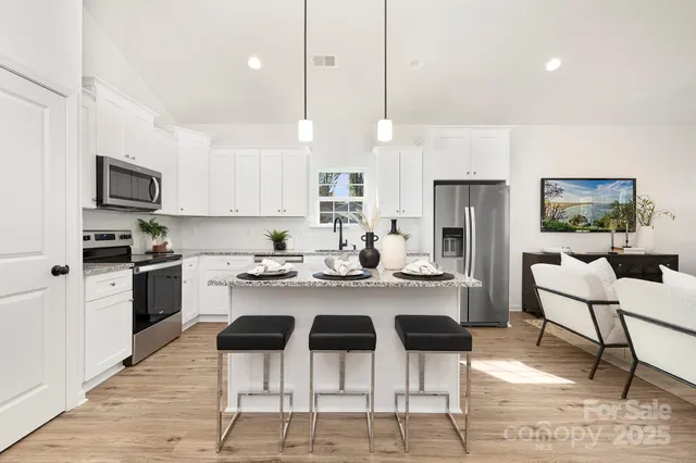 a kitchen with stainless steel appliances kitchen island granite countertop a refrigerator a stove a sink a dining table and chairs with wooden floor
