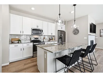 a kitchen with stainless steel appliances granite countertop a stove a sink a microwave a refrigerator a kitchen island a dining table and chairs