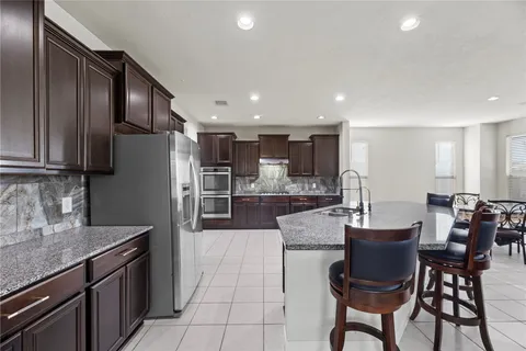 a kitchen with stainless steel appliances a dining table chairs refrigerator and sink