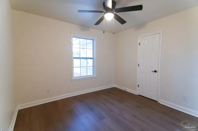 an empty room with wooden floor ceiling fan and windows