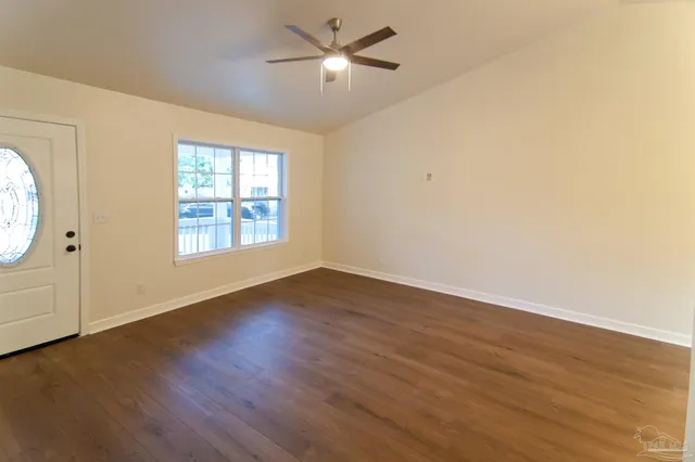an empty room with wooden floor chandelier fan and windows