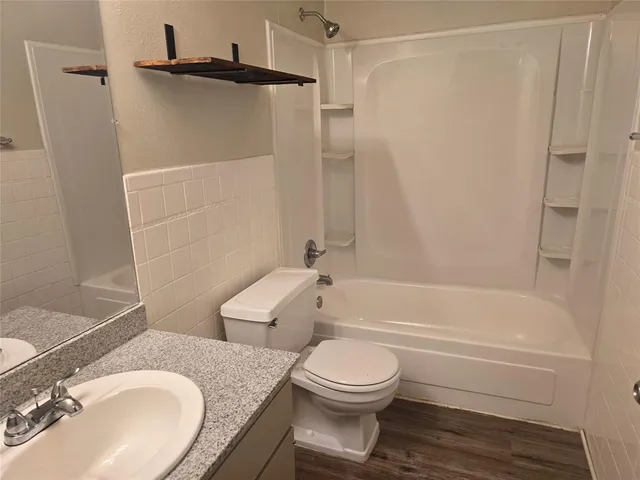 a bathroom with a granite countertop bathtub shower sink vanity and toilet
